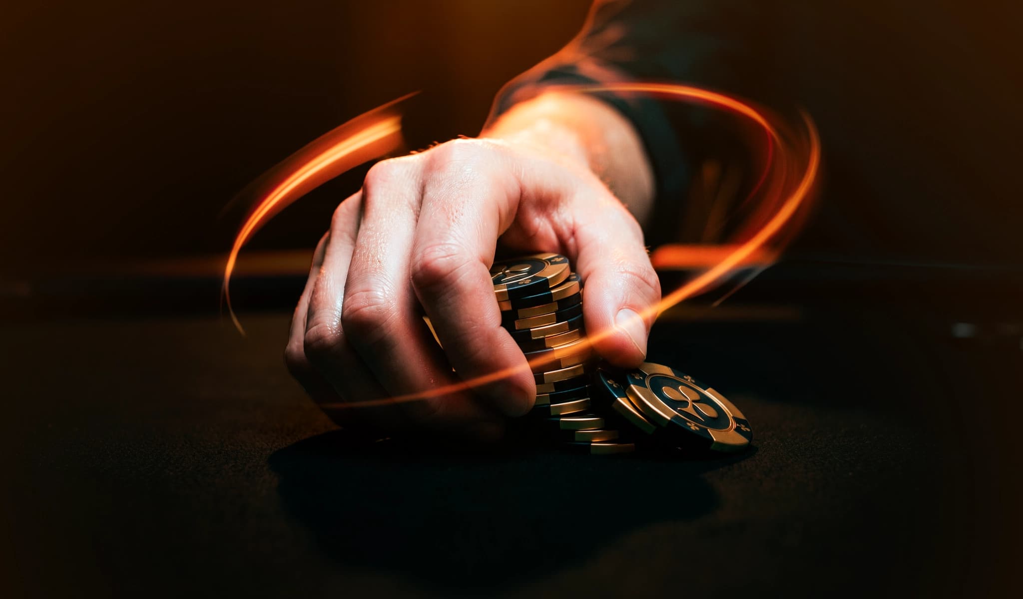 A hand grips a stack of poker chips, motion light trails swirling around it in the dark.