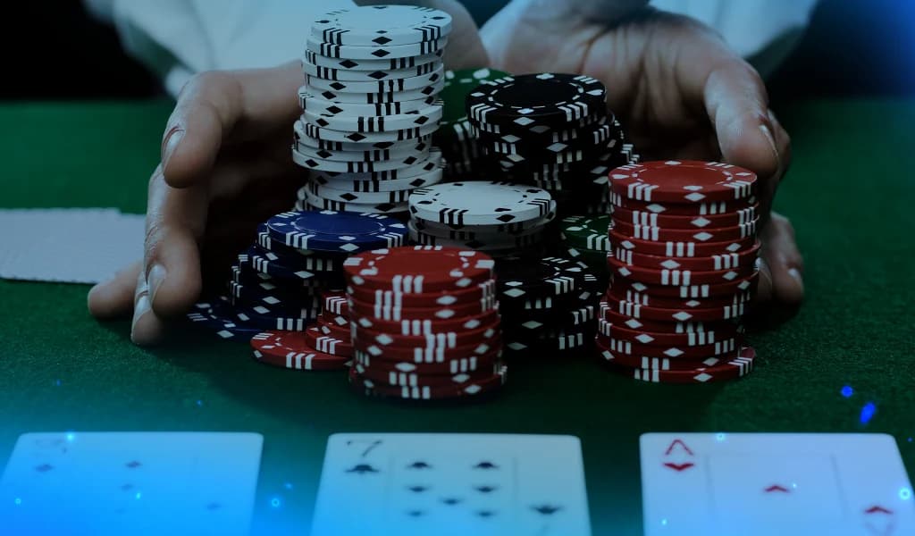 Hands pushing stacks of poker chips forward on a green table, with playing cards visible in the foreground.