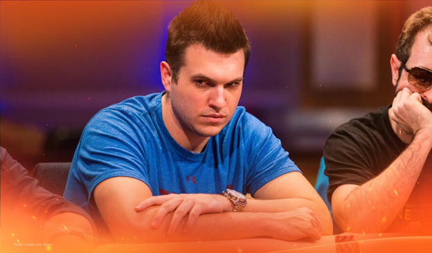 Doug Polk staring intensely at a poker table, wearing a blue shirt, with another player in sunglasses beside him.