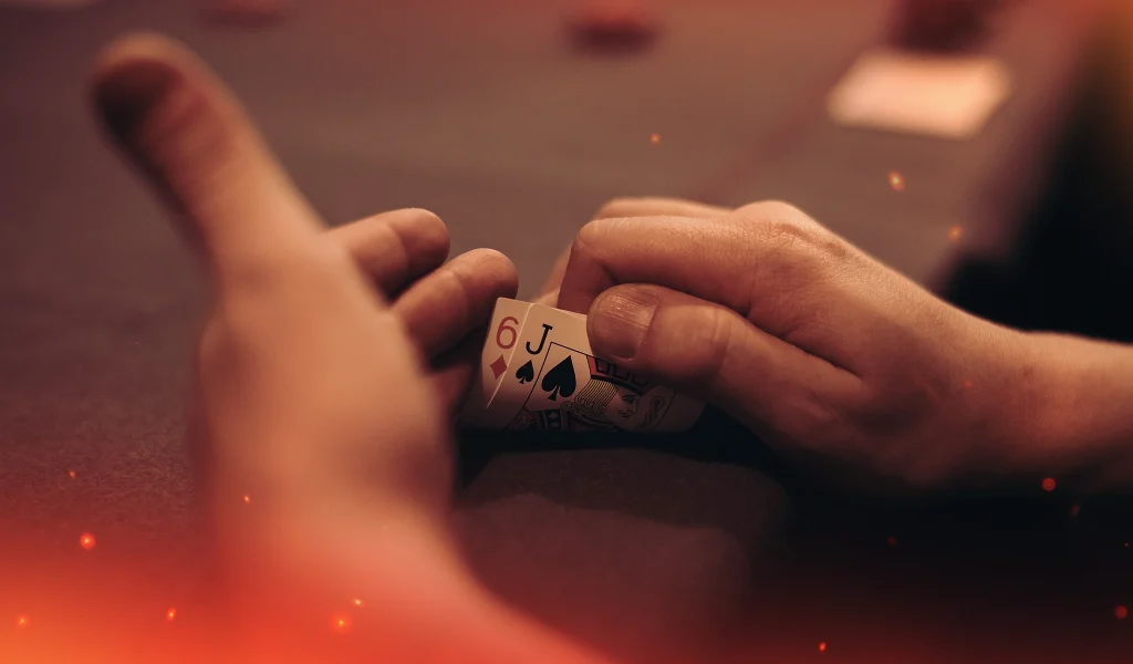 Close-up of a player peeling back hole cards showing Jack of Spades and Six of Diamonds at a poker table.
