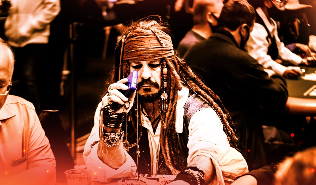 Man dressed as Jack Sparrow sitting at a poker table, holding a purple phone, surrounded by other players.