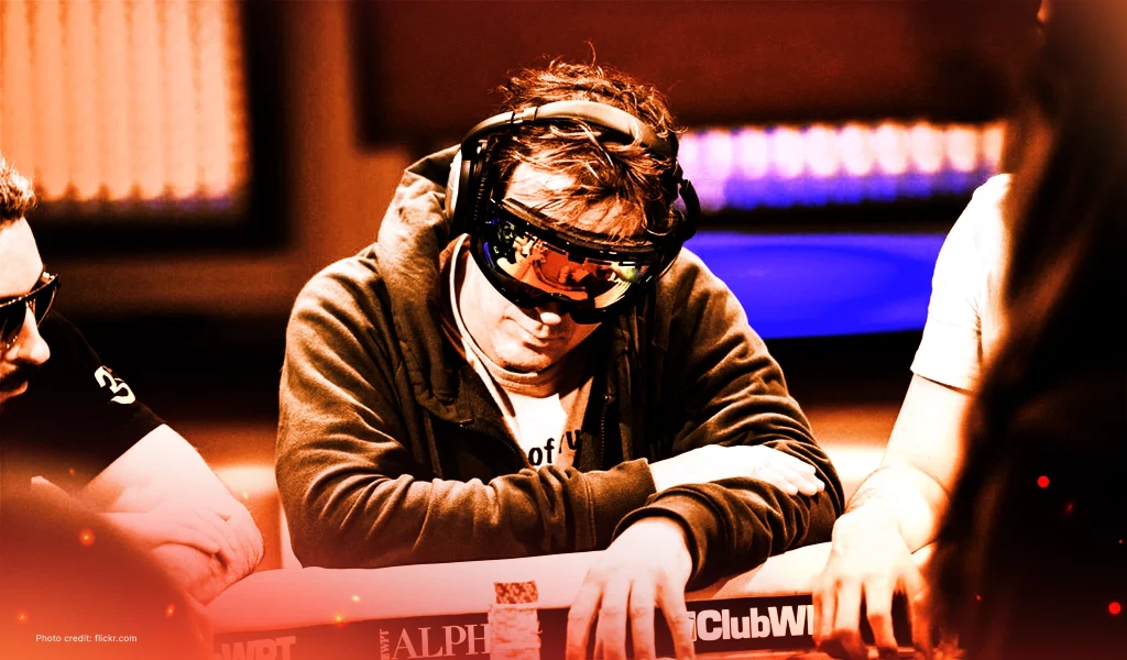 Phil Laak at a poker table wearing ski goggles and headphones, head tilted down as he moves chips.