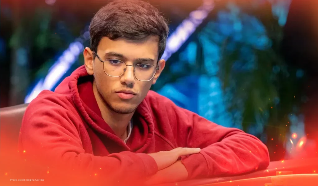 Samuel Mullur in a red hoodie leaning on a poker table, looking down in concentration