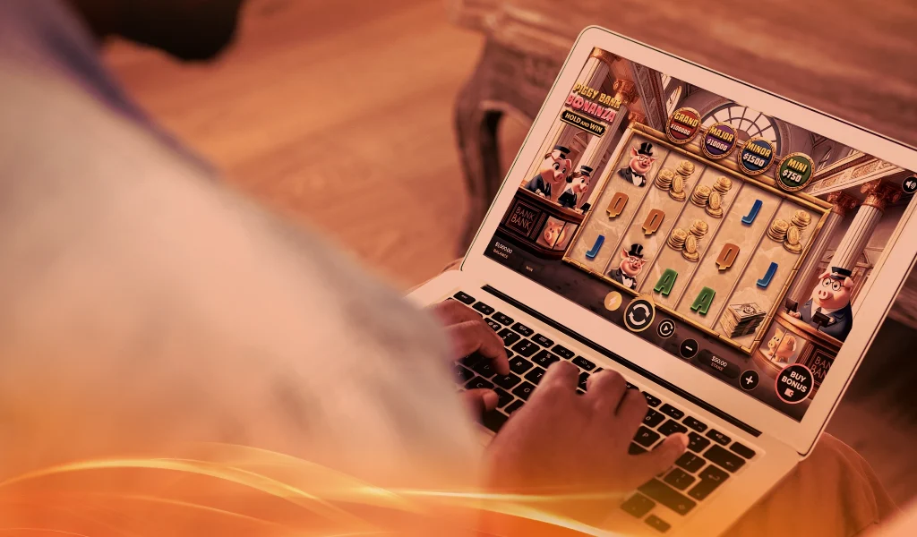 Close-up of a person playing Piggy Bank Bonanza slot game on a laptop, showing animated pig banker characters and gold coins.