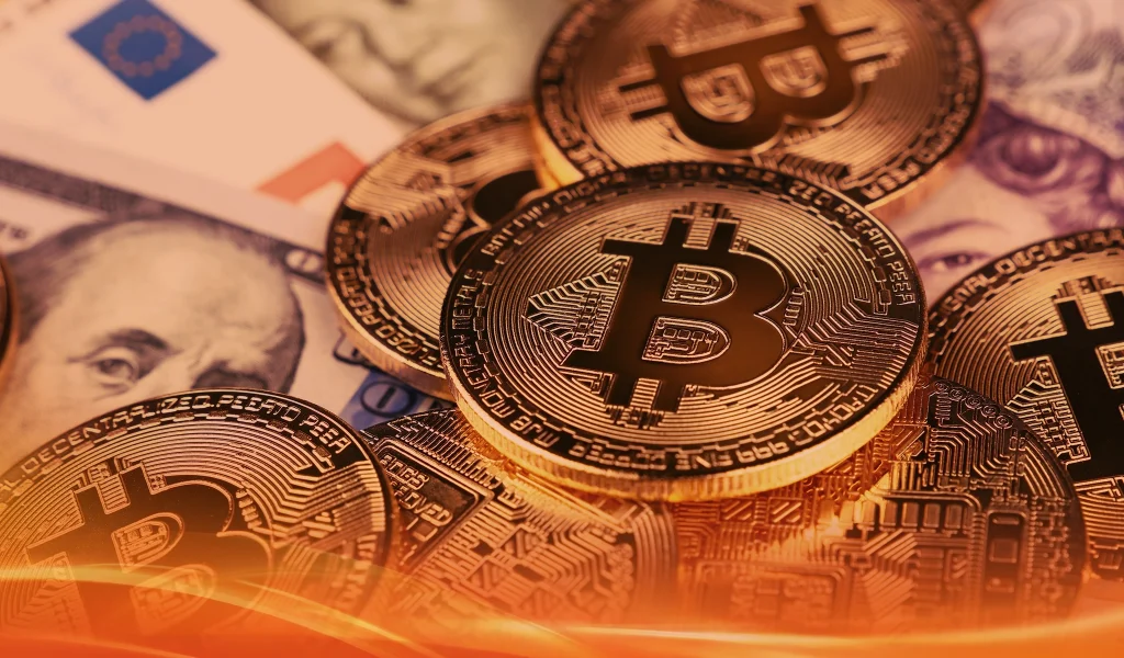 A close-up of stacked gold Bitcoin coins resting on a mix of U.S. dollar and euro banknotes.