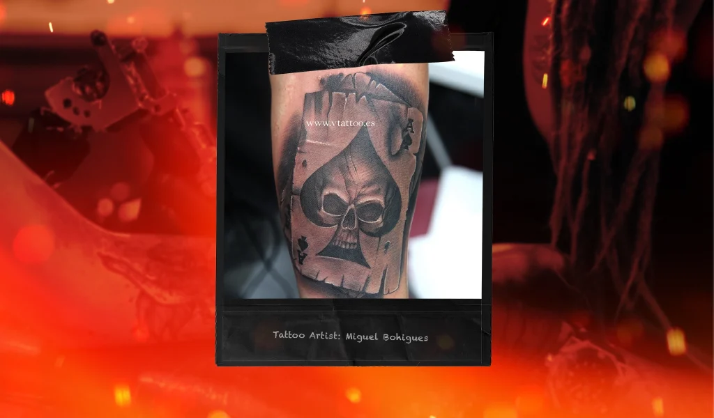 A black and gray tattoo of an Ace of Spades card with a skull design, surrounded by shading and texture.