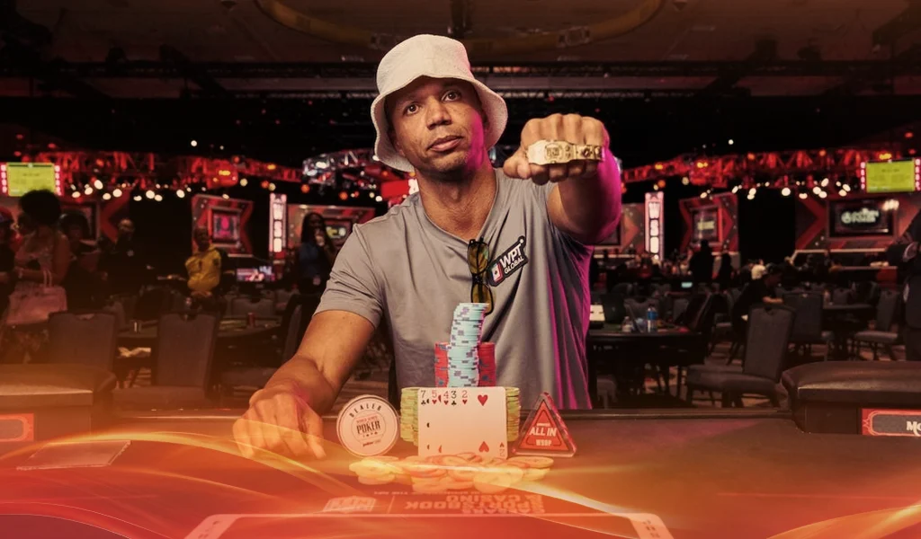 Phil Ivey wearing bucket hat shows gold ring, with poker chips and cards on table, WSOP event in background.